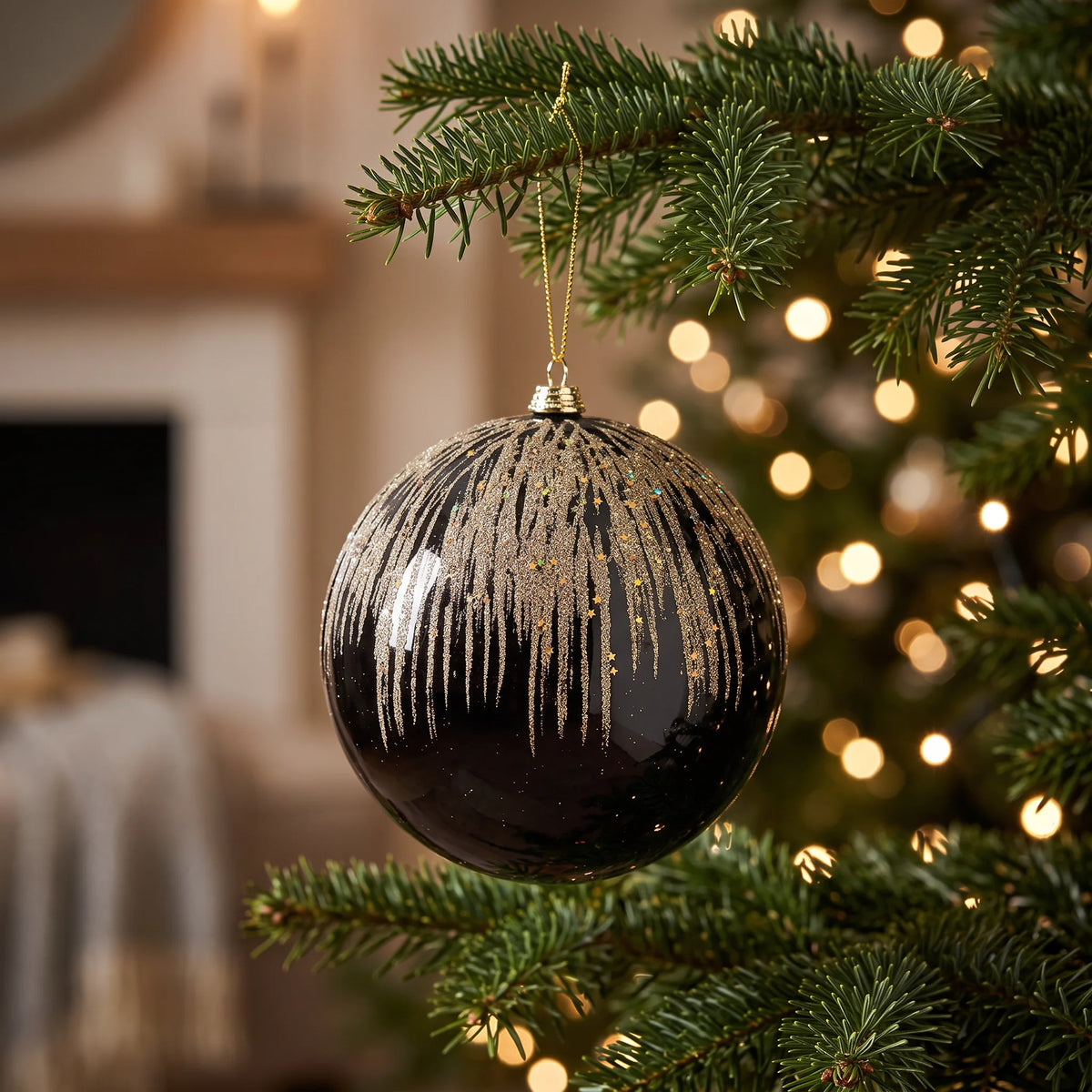 Black & Gold Glitter Drip Bauble - 15cm, hanging on a Christmas tree with warm white fairy lights, featuring a glossy black finish and cascading gold glitter detailing.