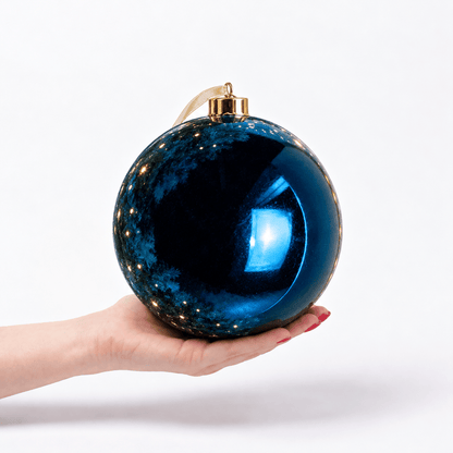 Blue Shiny Large Bauble – 20cm, oversized metallic blue Christmas bauble resting in a hand to demonstrate its 25cm diameter, featuring a high-shine reflective finish and gold hanging cap.