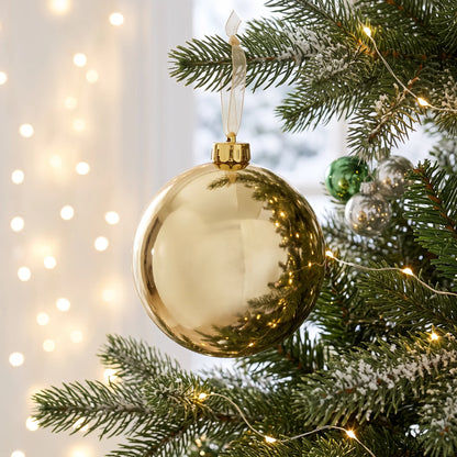 15cm champagne shiny Christmas bauble hanging on a festive tree with frosted branches, silver and green ornaments and warm white fairy lights