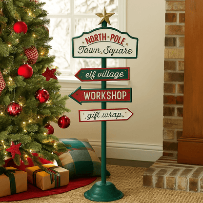 North Pole Signpost 46cm Christmas decoration featuring colourful directional signs and a gold star, displayed beside a Christmas tree with red baubles, warm fairy lights and wrapped presents.