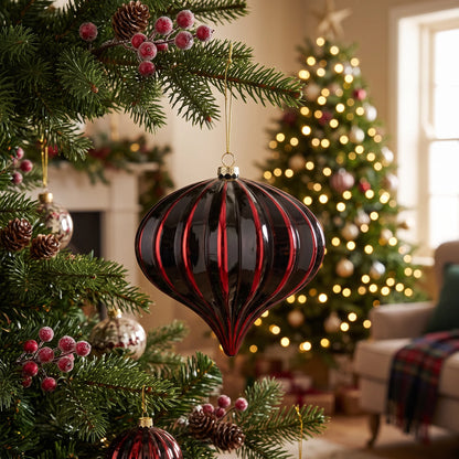 Luxury black and red onion Christmas bauble hanging on a festive Christmas tree decorated with warm white fairy lights, red berries and pine cones.